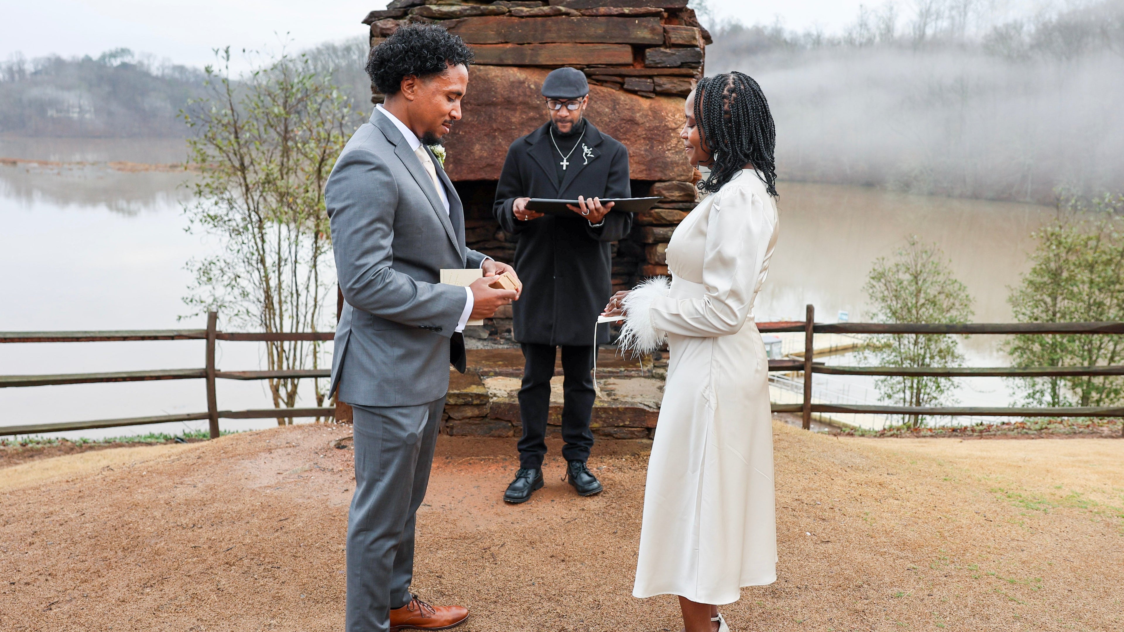 Two people standing in front of a wooden structure by a lake, with a third person holding a tablet.